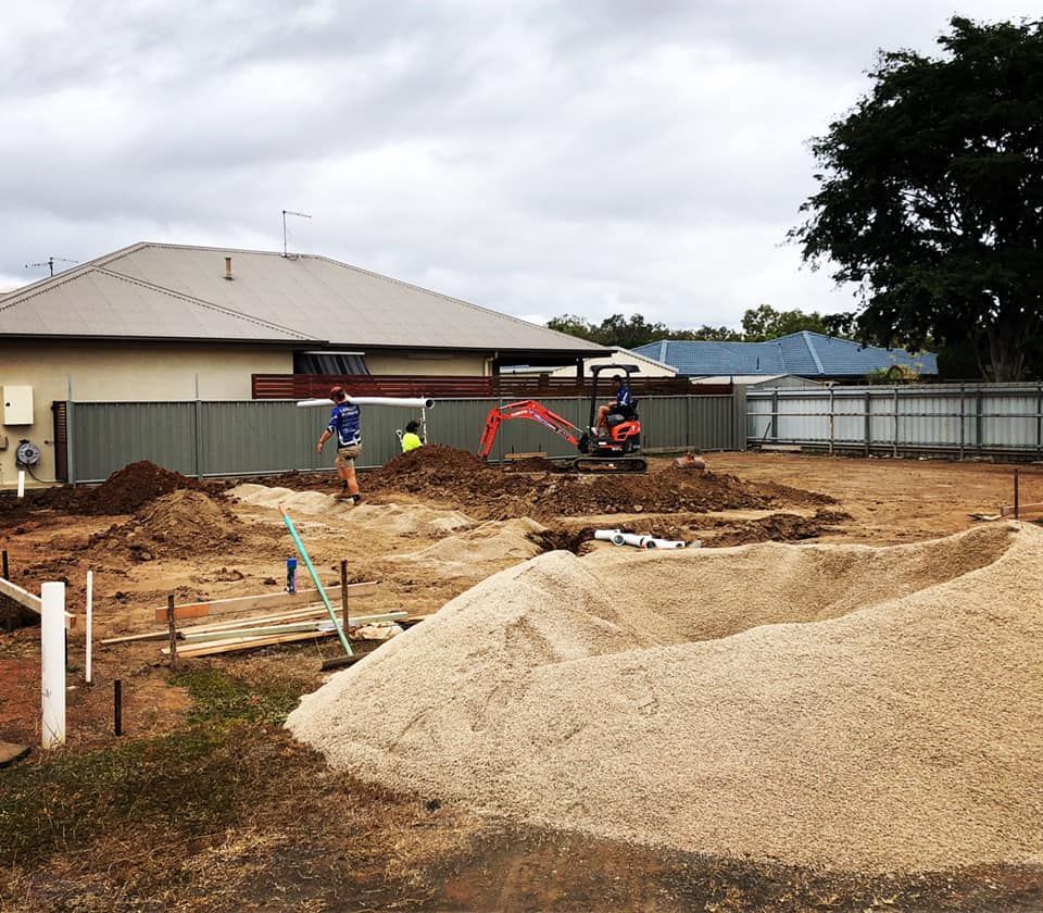 Construction Site With an Excavator Moving Dirt, Workers, and a Large Pile of Gravel — Langley Plumbing in Mareeba, QLD