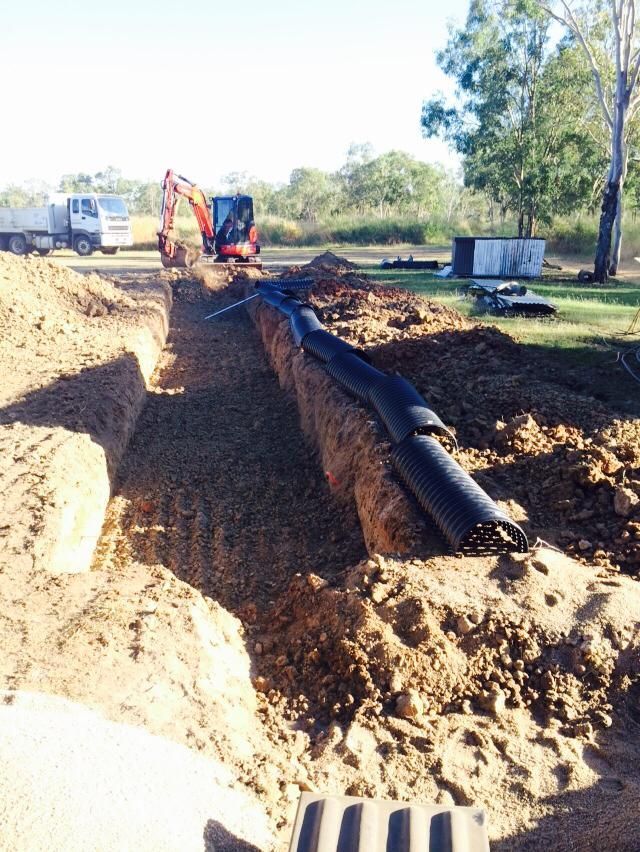 Trench with black pipe, mini excavator, and truck on a construction site outdoors — Langley Plumbing in Mareeba, QLD