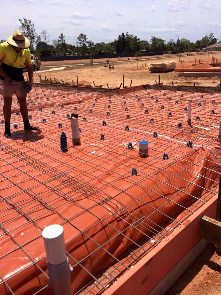 Construction Worker on a Site With Rebar Grid, Plumbing Pipes, and Orange Underlayment — Langley Plumbing in Mareeba, QLD