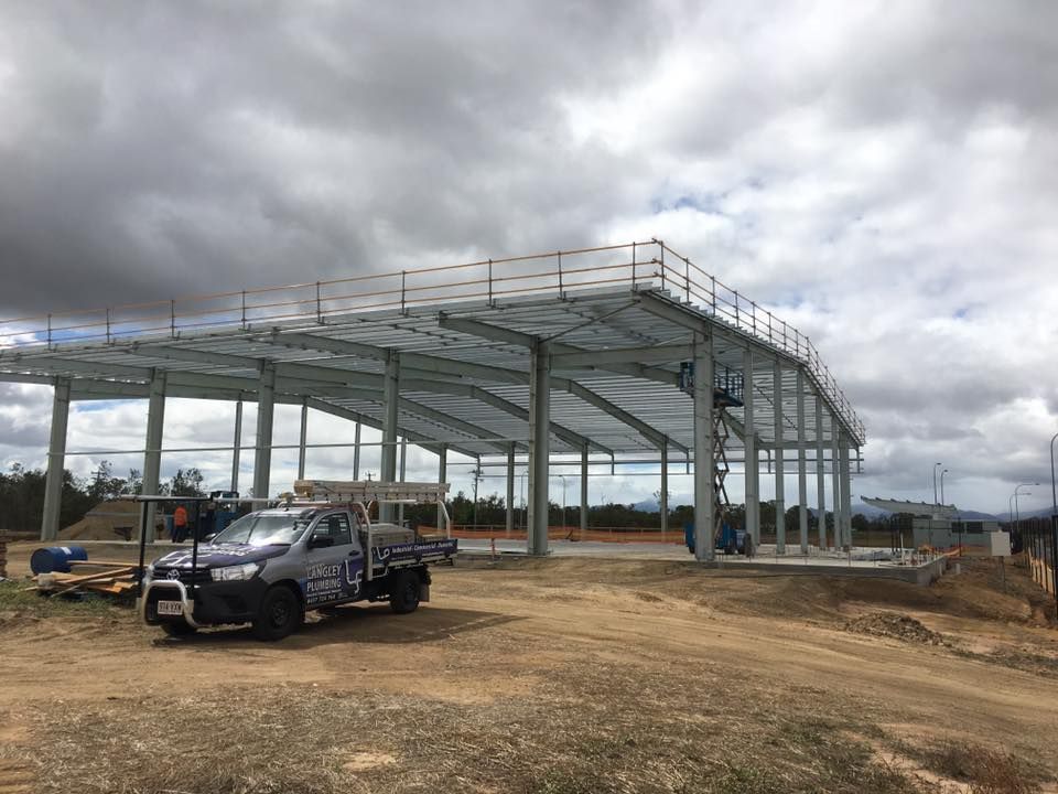 A Person Installing Plumbing Near a Row of Black Salon Sinks on a Wooden Floor — Langley Plumbing in Mareeba, QLD