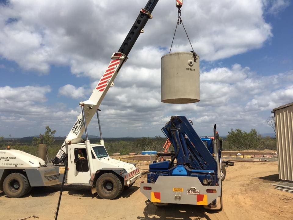 Crane lifting a cylindrical concrete tank at a construction site on a sunny day — Langley Plumbing in Mareeba, QLD