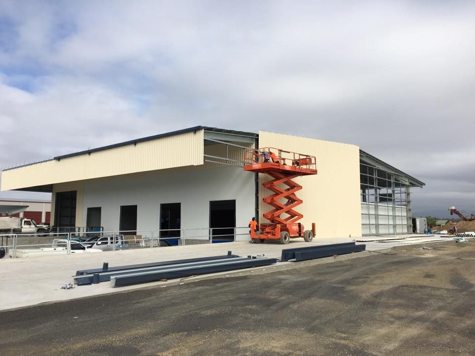 Construction of a white and beige building; an orange lift is raised near the side wall — Langley Plumbing in Mareeba, QLD