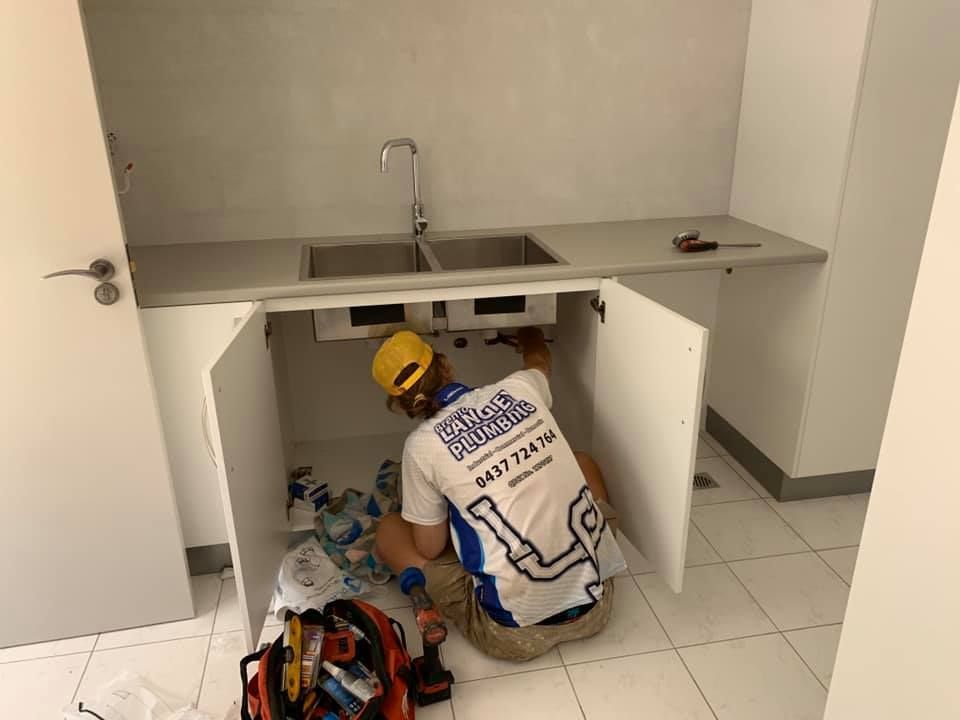 Plumber Installing Pipes Under a Kitchen Sink in a White Cabinet — Langley Plumbing in Mareeba, QLD
