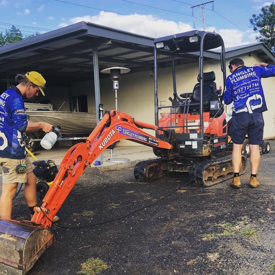 Two People Cleaning a Small Orange Kubota Excavator — Langley Plumbing in Mareeba, QLD