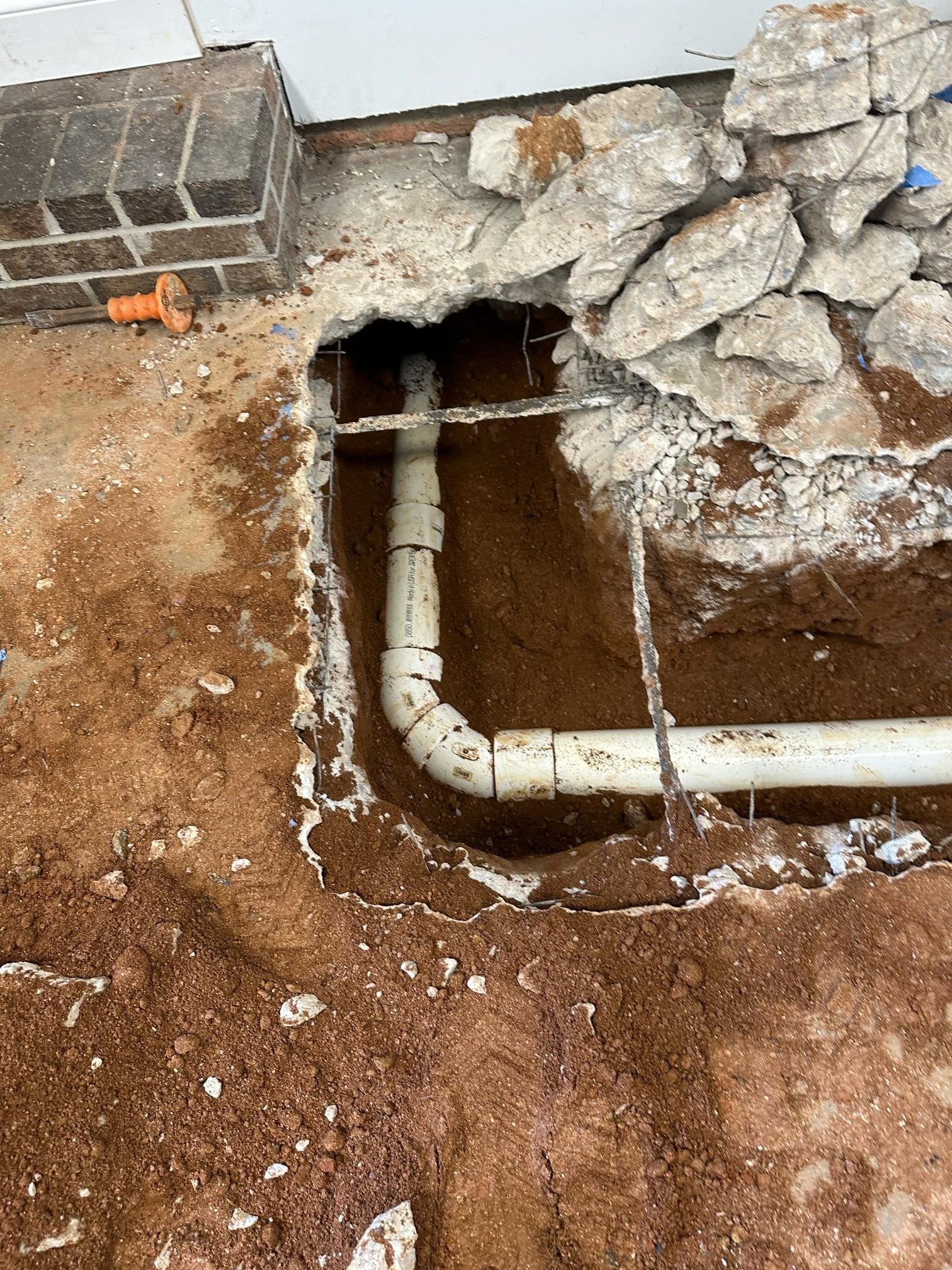 Exposed PVC drain pipes in excavated ground. Concrete and bricks are visible. Brown soil surrounds the pipes.