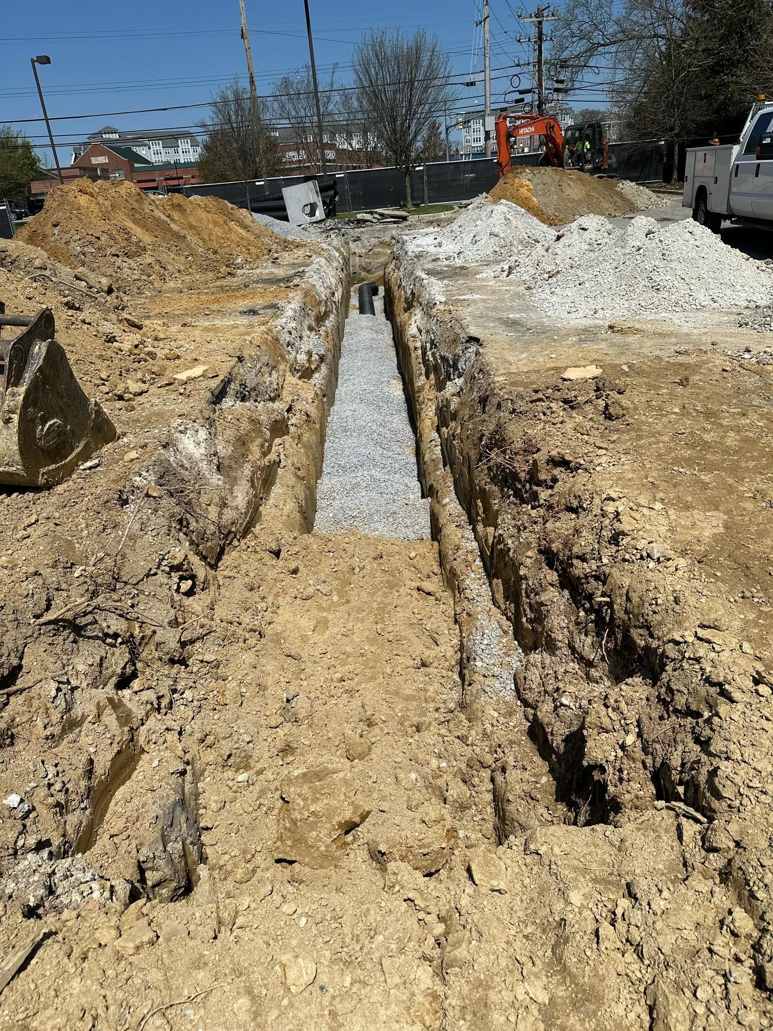 A trench dug in the ground, filled with gravel, construction site.