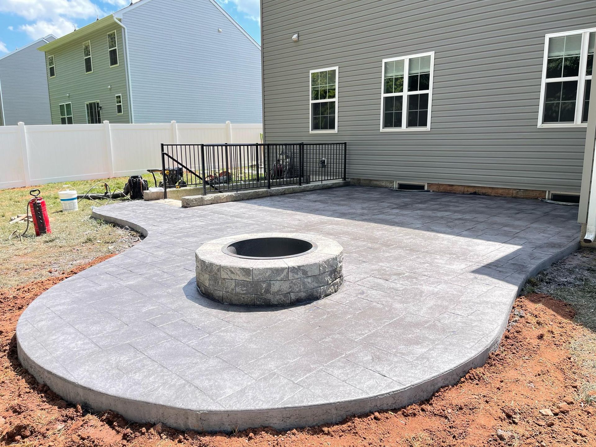 A concrete patio with a fire pit, adjacent to a gray house. Construction in progress.