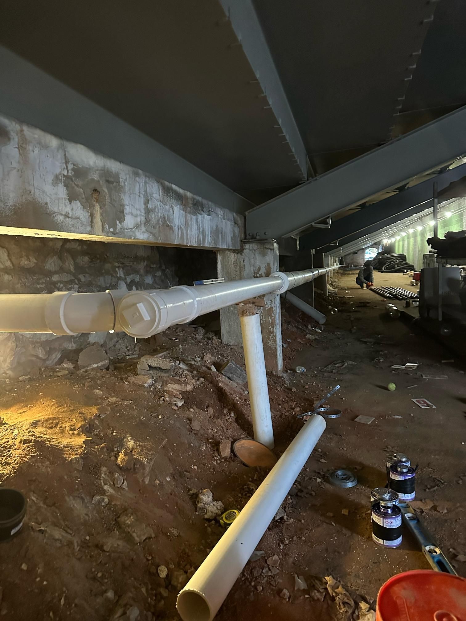 White PVC pipes under a bridge. Construction site with exposed dirt and beams.