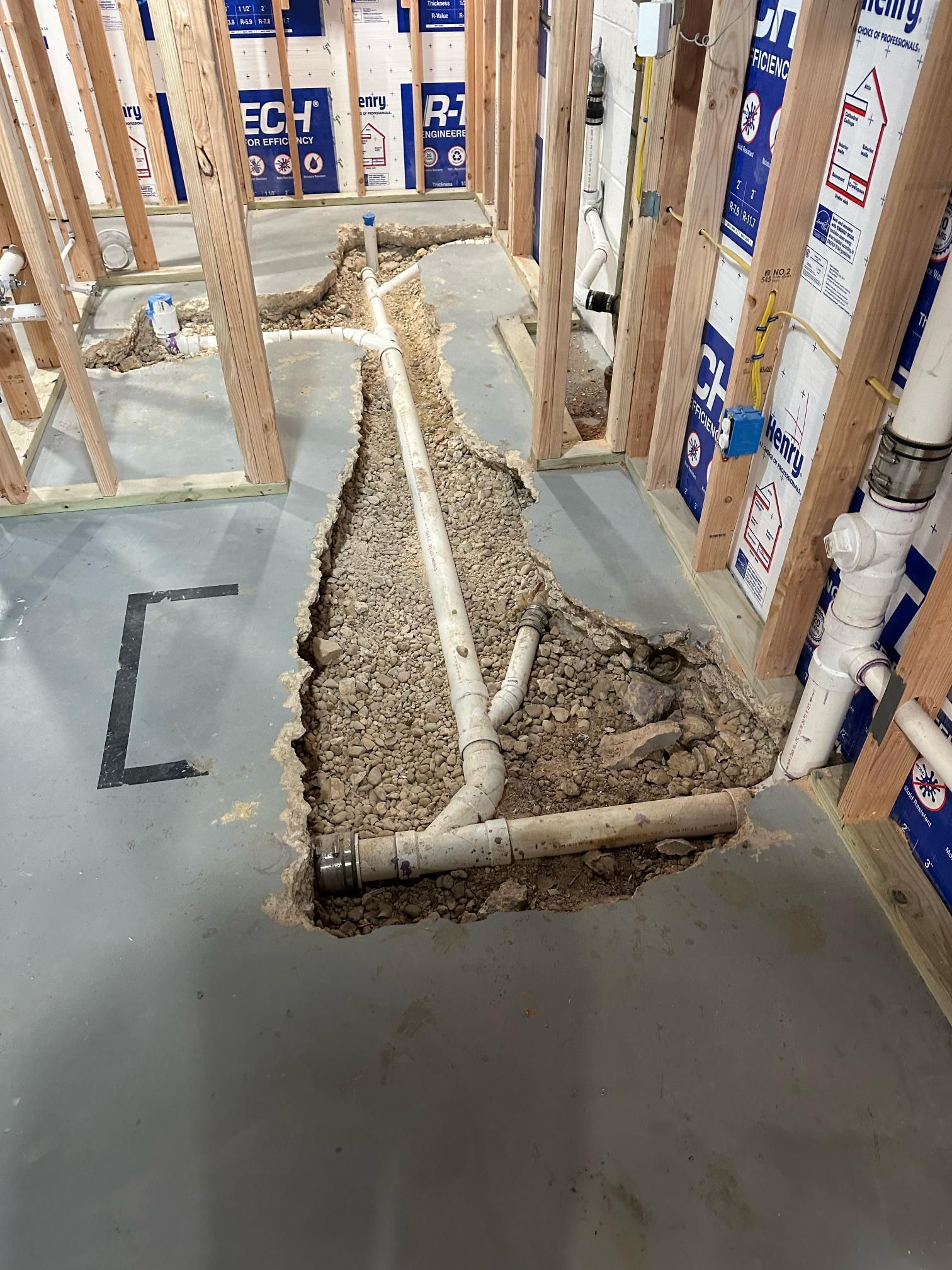 Construction site: Plumbing pipes in a trench dug into the concrete floor, framed walls surround.