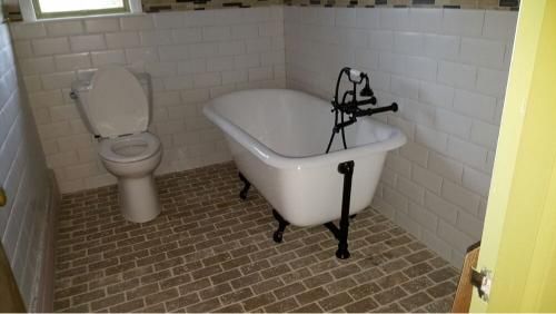 Bathroom with white tile walls, brick-pattern floor, a clawfoot tub, and a toilet.
