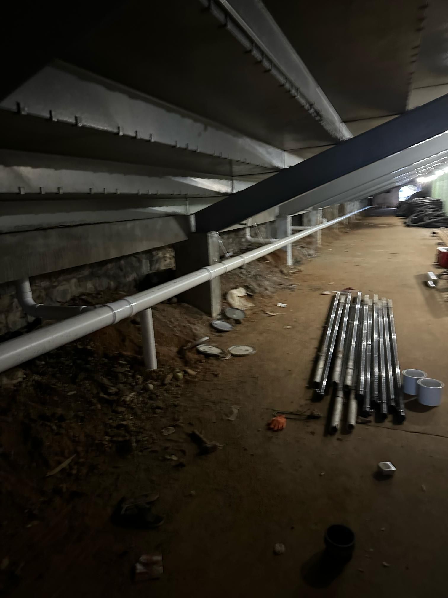 Underground construction with PVC pipes along the wall, pipes on the ground, and a dark, unfinished setting.