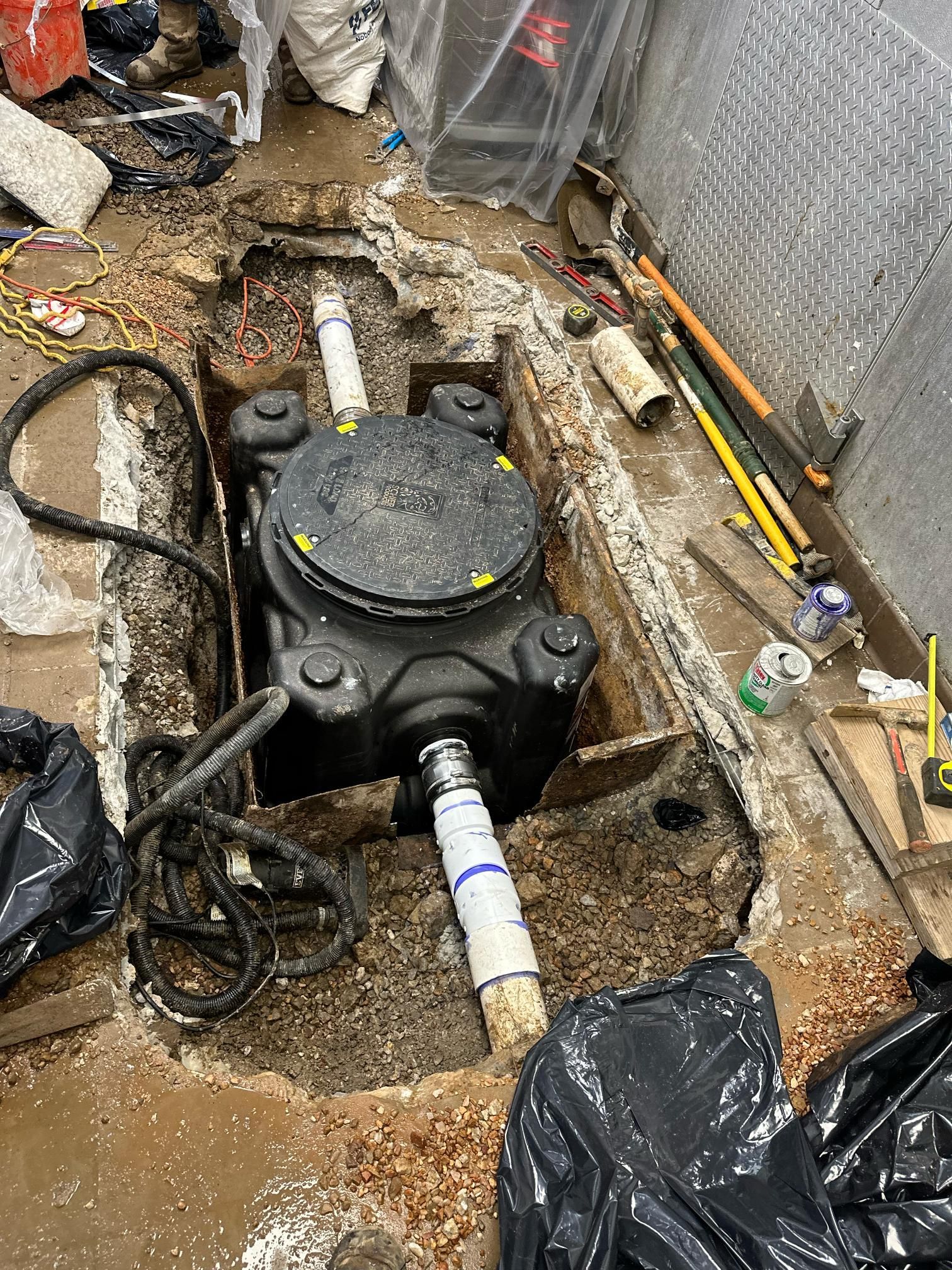 Black sump pump installed in a hole in a concrete floor with pipes and debris around.
