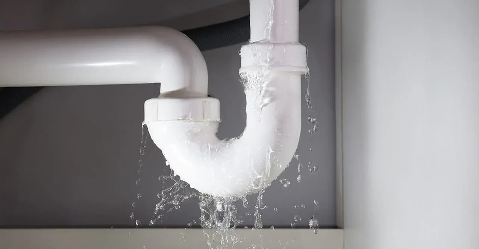 Leaking white plumbing pipe under a sink, water dripping.