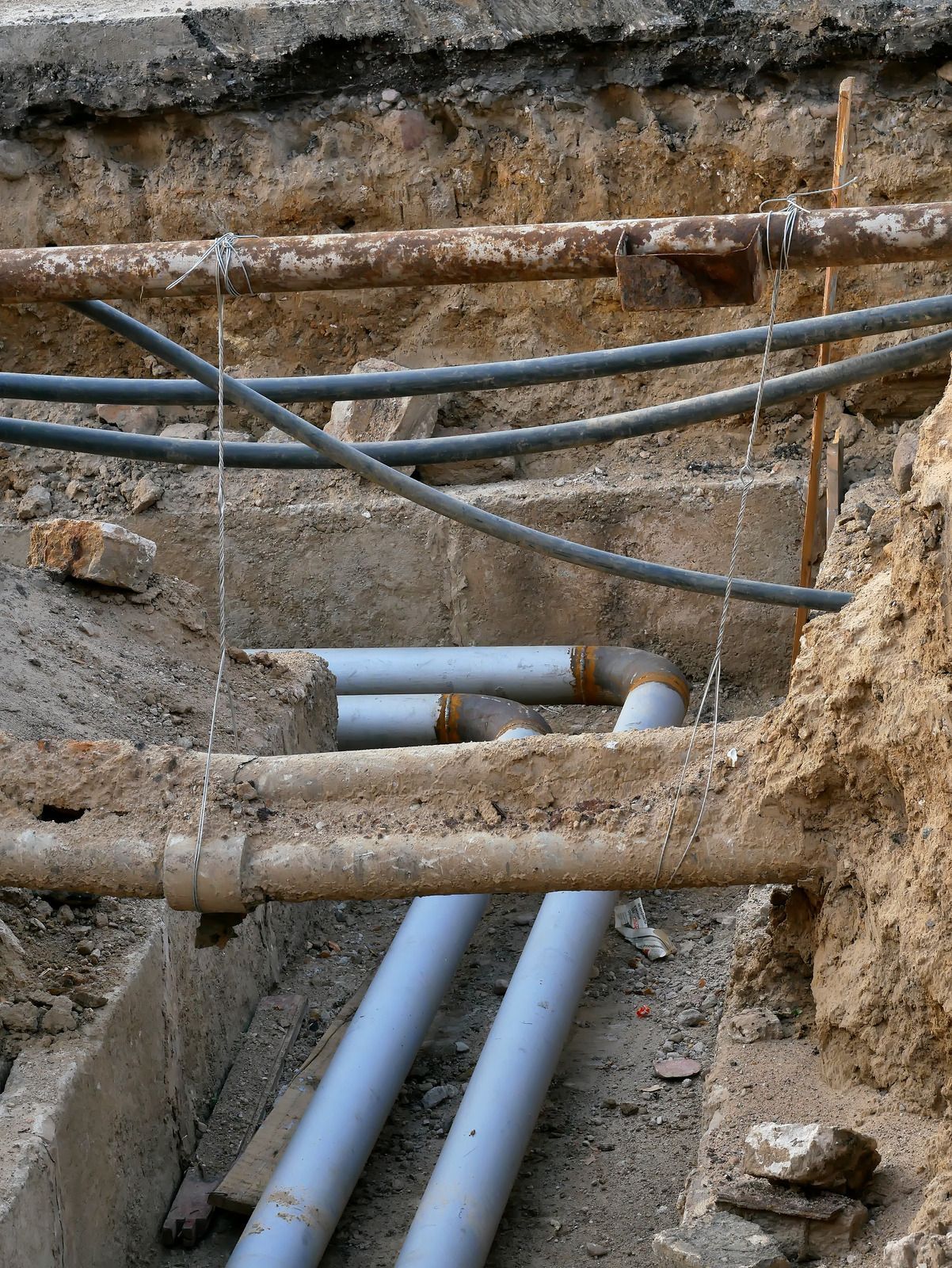 Pipes of various types and colors exposed in a trench.