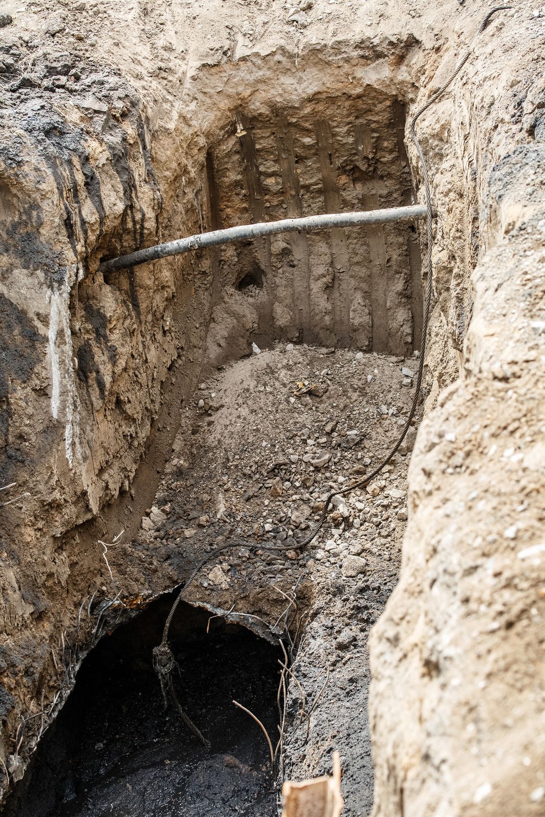 Trench with buried metal conduit, dirt walls, and dark bottom.