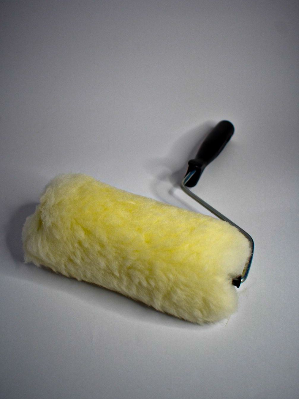 Rodillo de pintura amarillo con mango negro sobre fondo blanco.