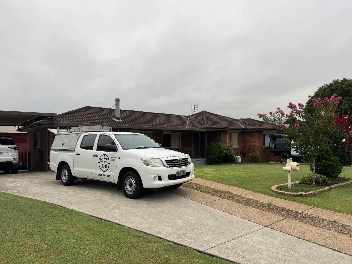 A white work truck parked on a driveway in front of a single-story brick house under a cloudy sky.