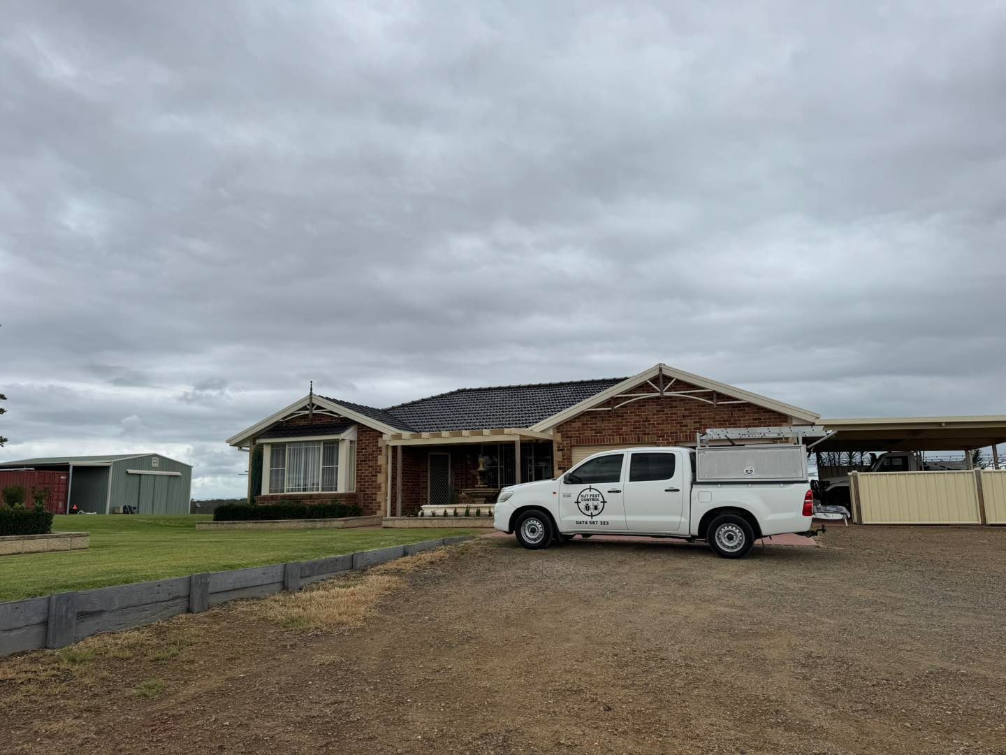 A white work truck parked on a gravel driveway in front of a brick house under a cloudy sky.