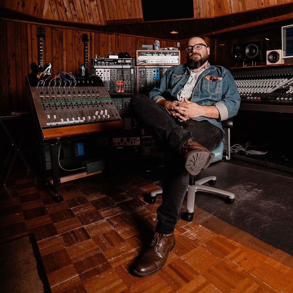 a man is sitting in a chair in a recording studio.