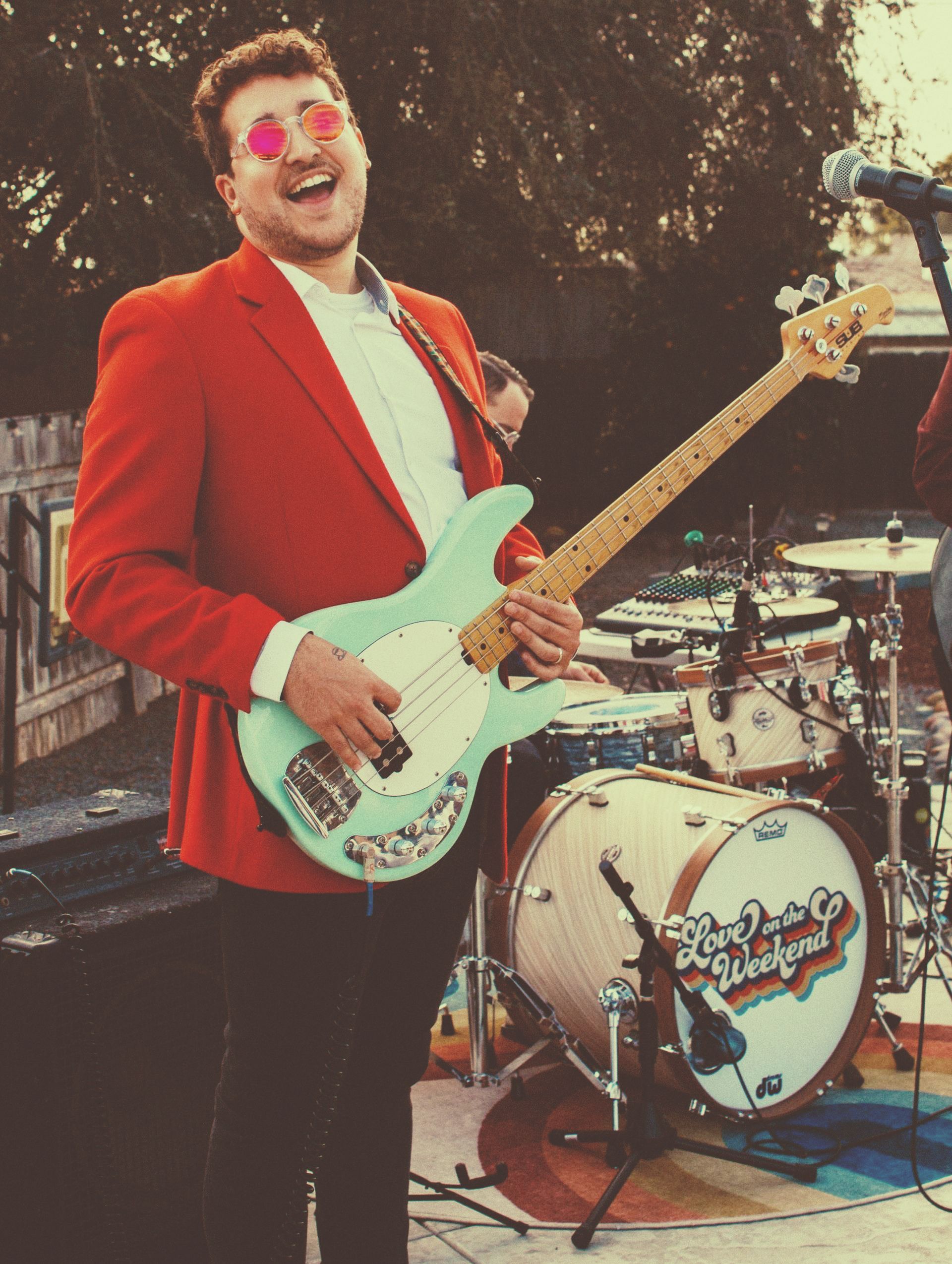a man in a red jacket is playing a bass in front of a drum set