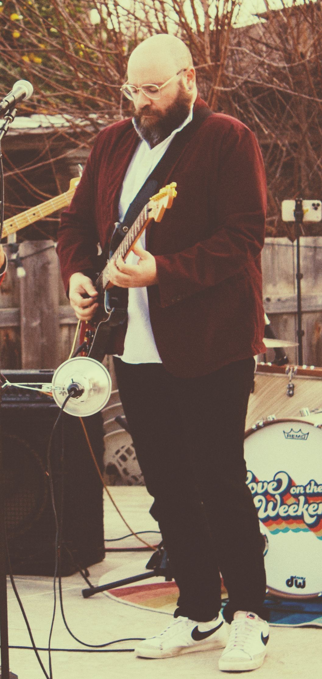a man with a beard is playing a guitar in front of a drum set.