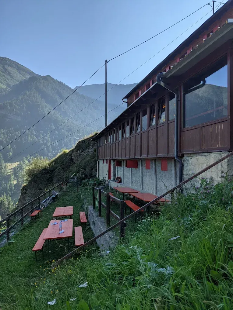 Un grande edificio con molte finestre, tavoli e panche di fronte.