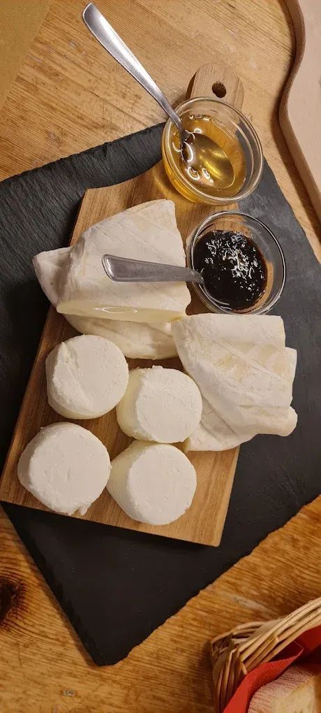 Un tagliere di legno sul quale sono disposti vari formaggi e marmellate.