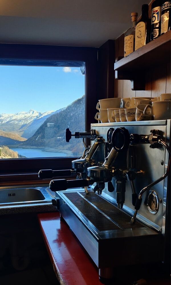Una macchina per il caffè è appoggiata su un bancone davanti a una finestra con le montagne sullo sfondo.