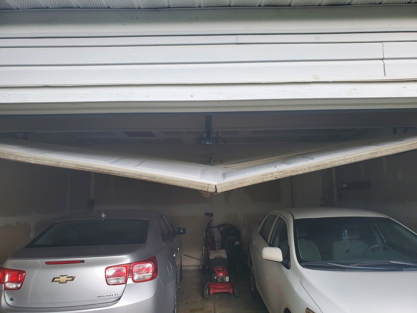 Two cars are parked in a garage with the door open.