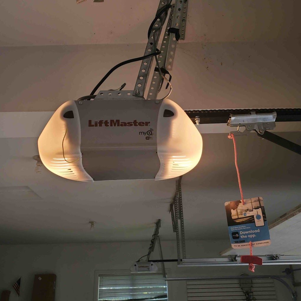 A lift master garage door opener is hanging from the ceiling of a garage.