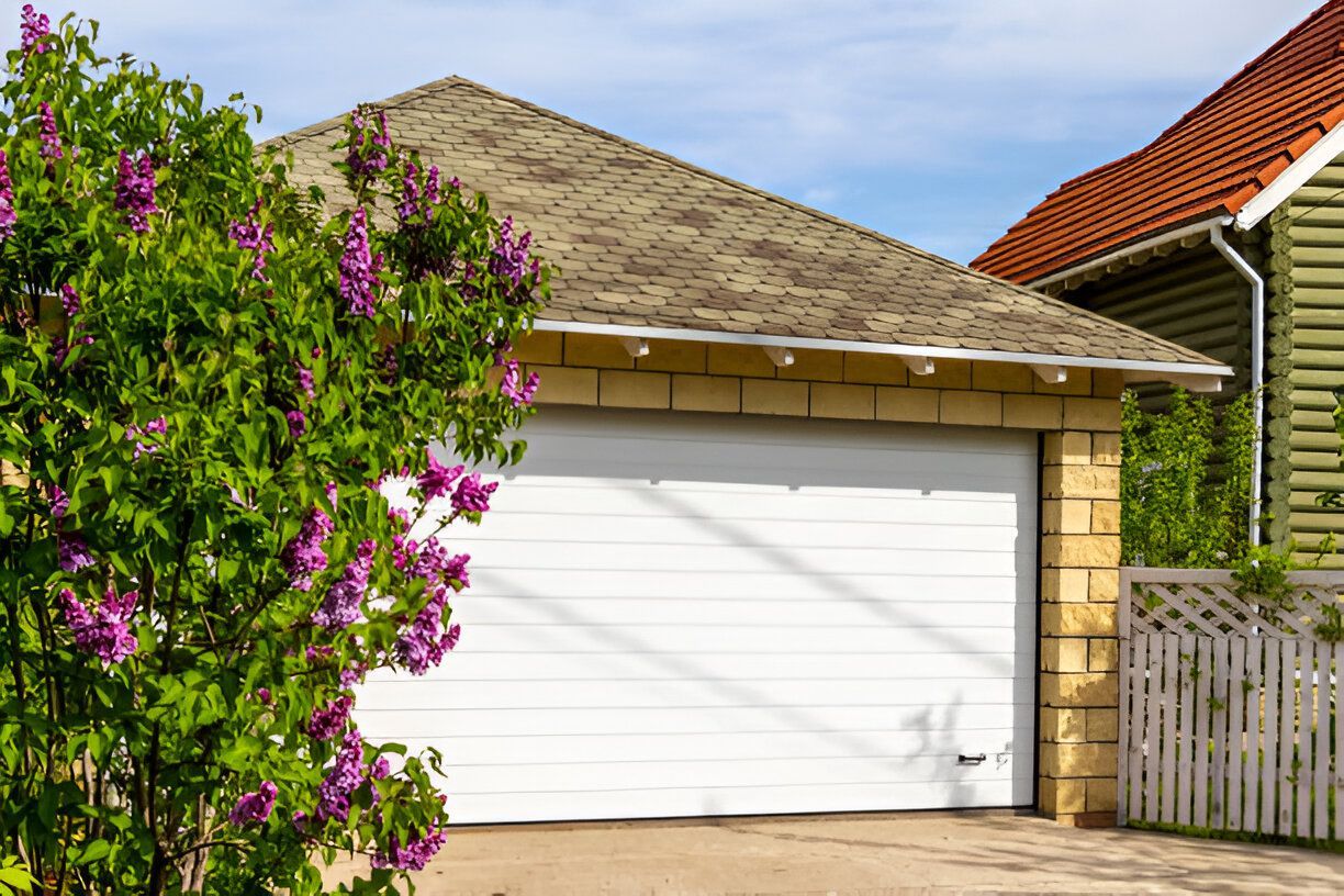A white garage door with purple flowers in front of a house