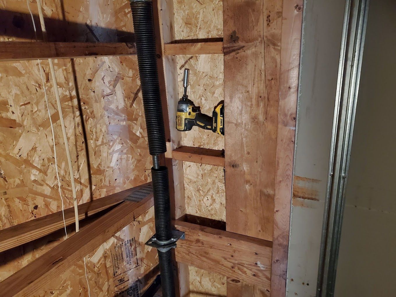 A drill is sitting on a wooden wall next to a garage door spring.