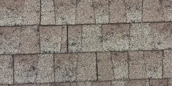 A close-up view of textured, rectangular gray and brown asphalt roofing shingles arranged in an overlapping pattern.