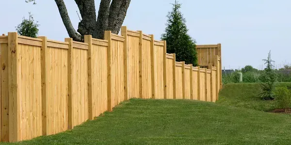 A wooden privacy fence follows the slope of a grassy hill outdoors on a sunny day.