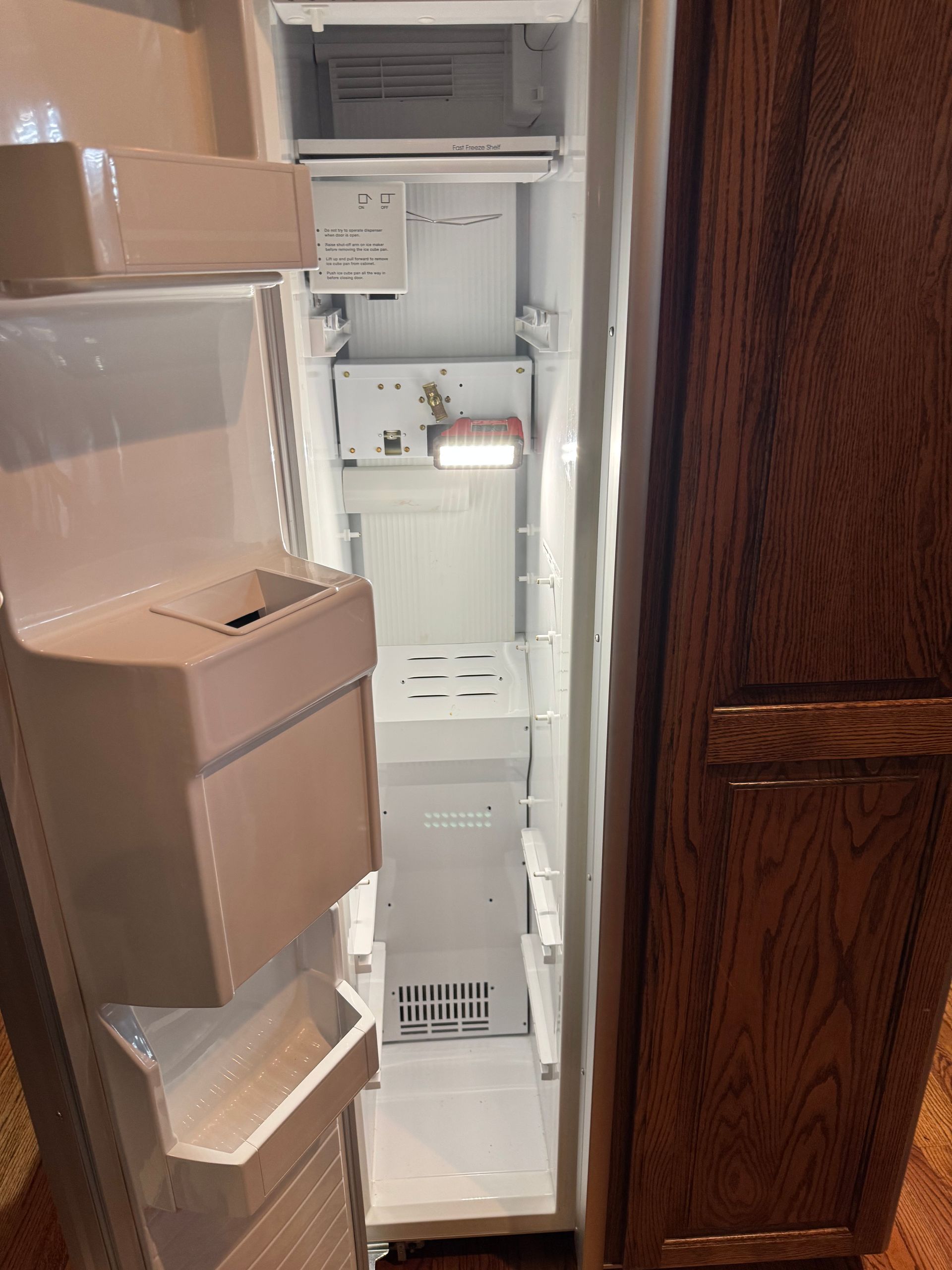 An empty refrigerator interior with the door open. White shelves and drawers inside. Wooden door frame on right.