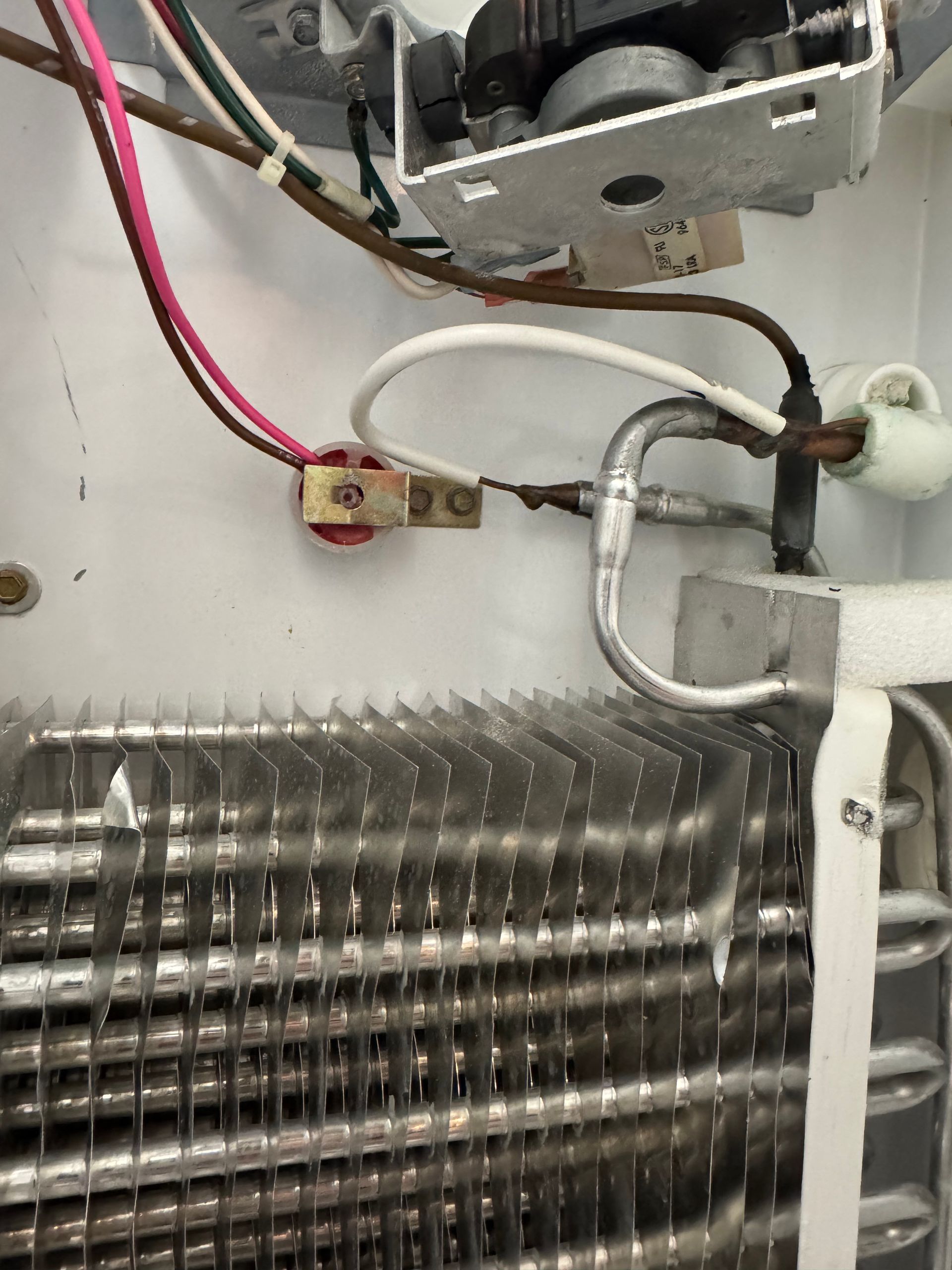Refrigerator coils and wiring. White interior, silver coils, and various colored wires connected to a terminal block.