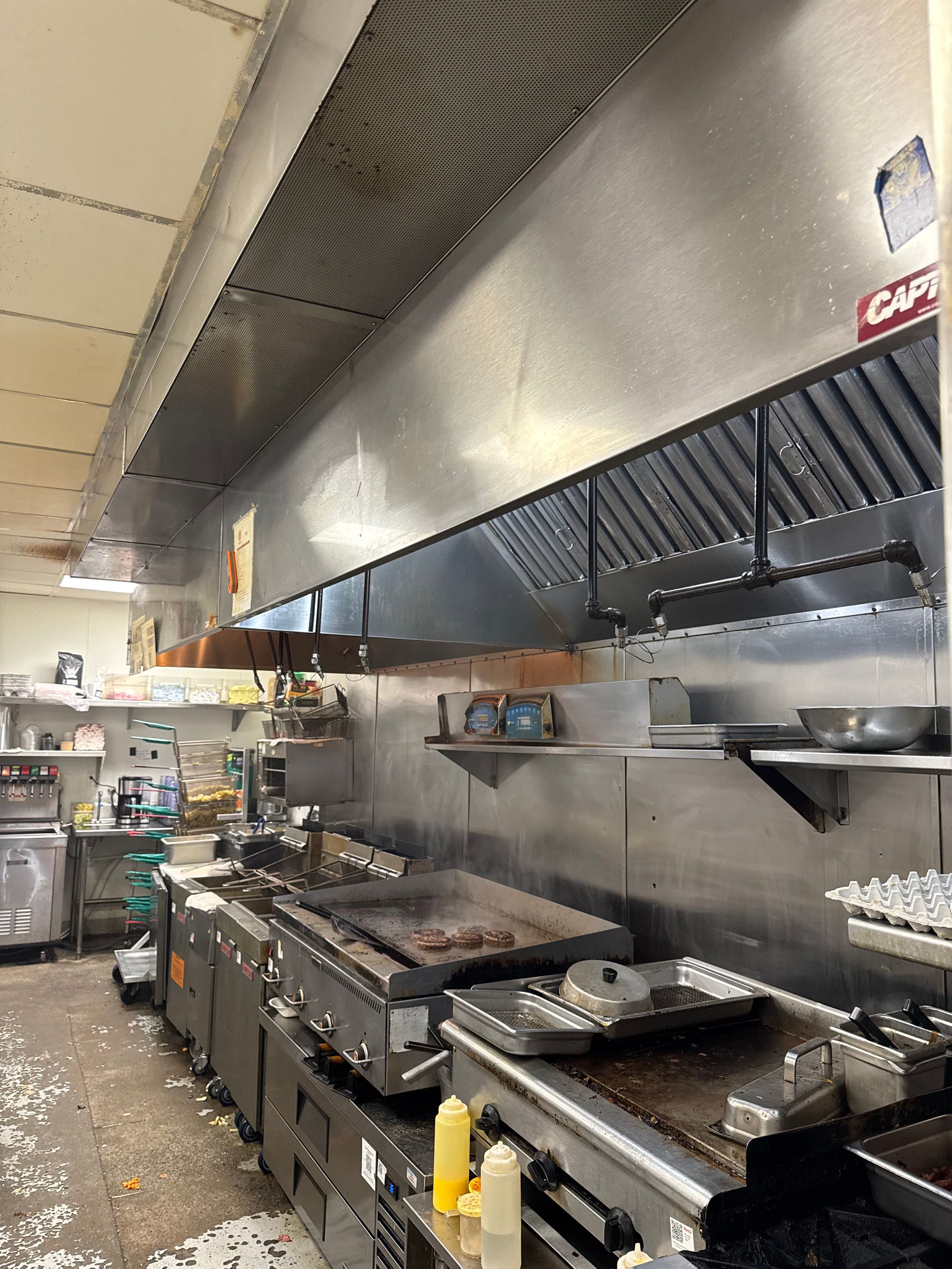Commercial kitchen with stainless steel appliances, griddles, and a ventilation hood.