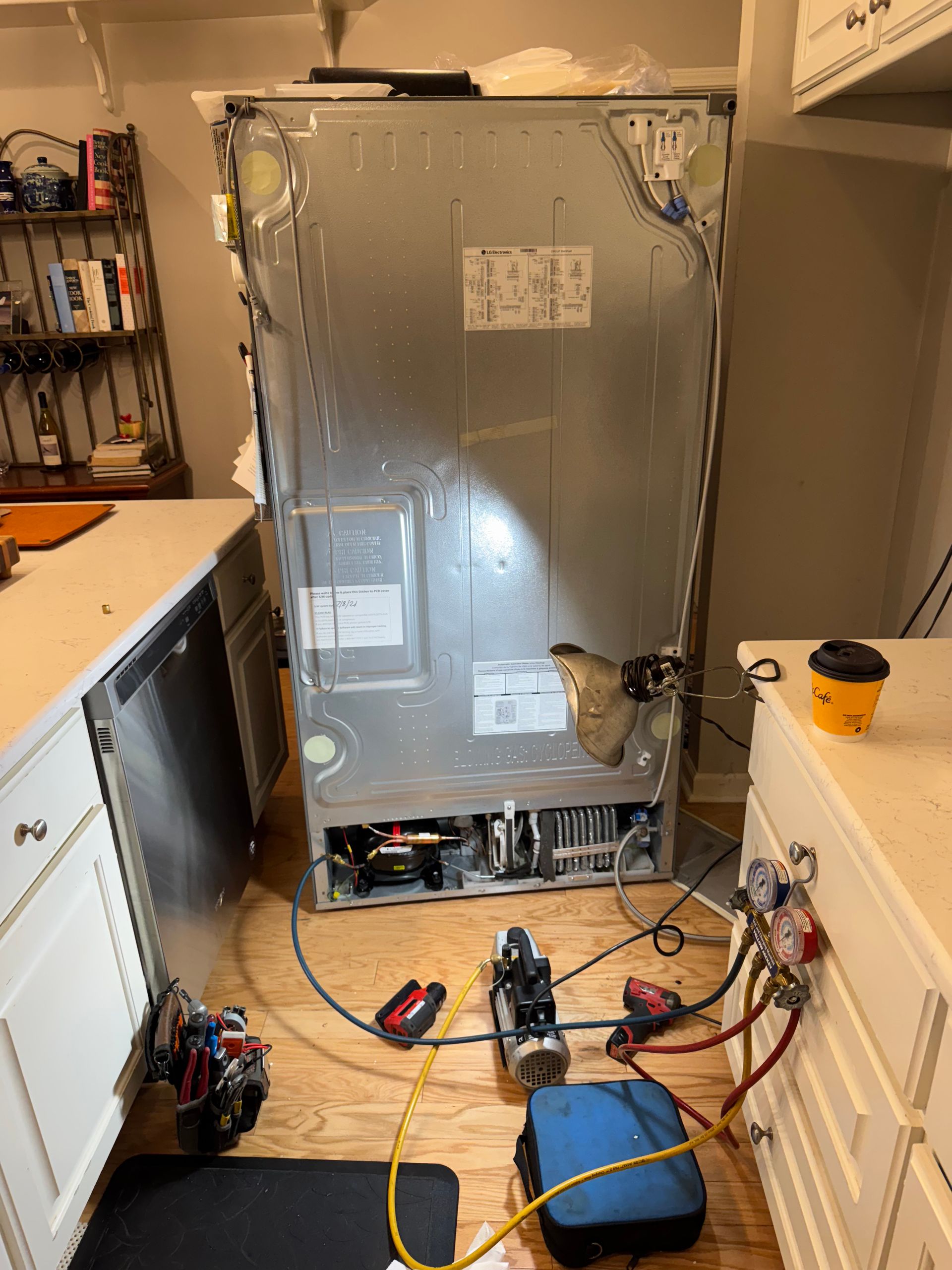 Refrigerator repair: Back view of a refrigerator with hoses and equipment attached in a kitchen setting.