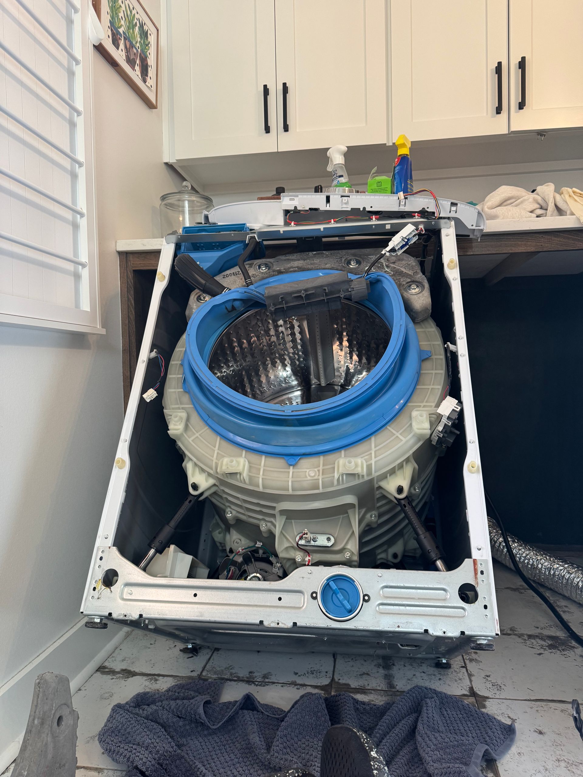 Washing machine, disassembled, showing internal drum. Blue rubber ring around opening, in a laundry room setting.