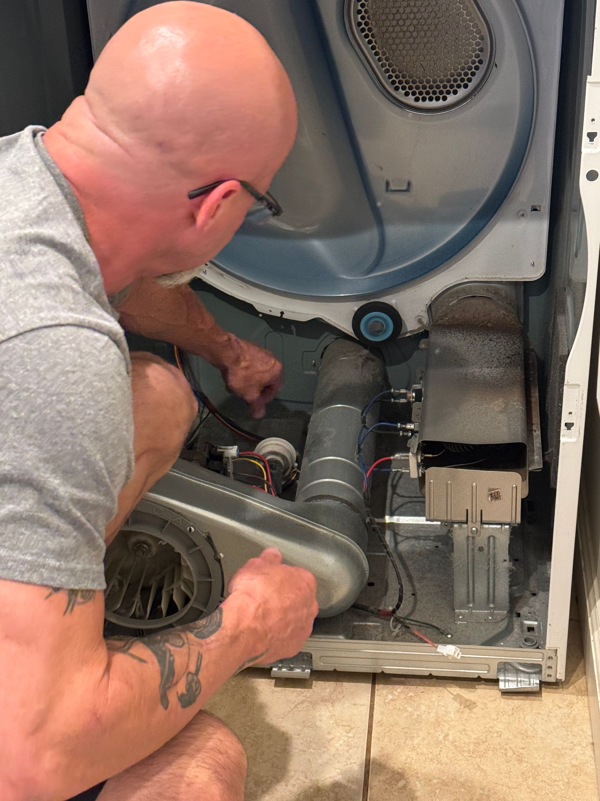 Man inspecting the interior of a dryer with the back panel removed, examining the vent and components.