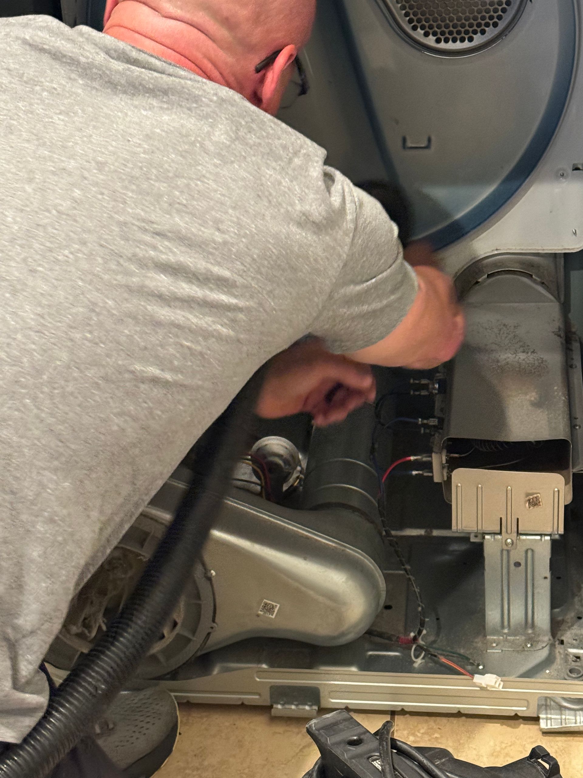 Person working on the interior of a dryer, visible are parts like vent and wires.