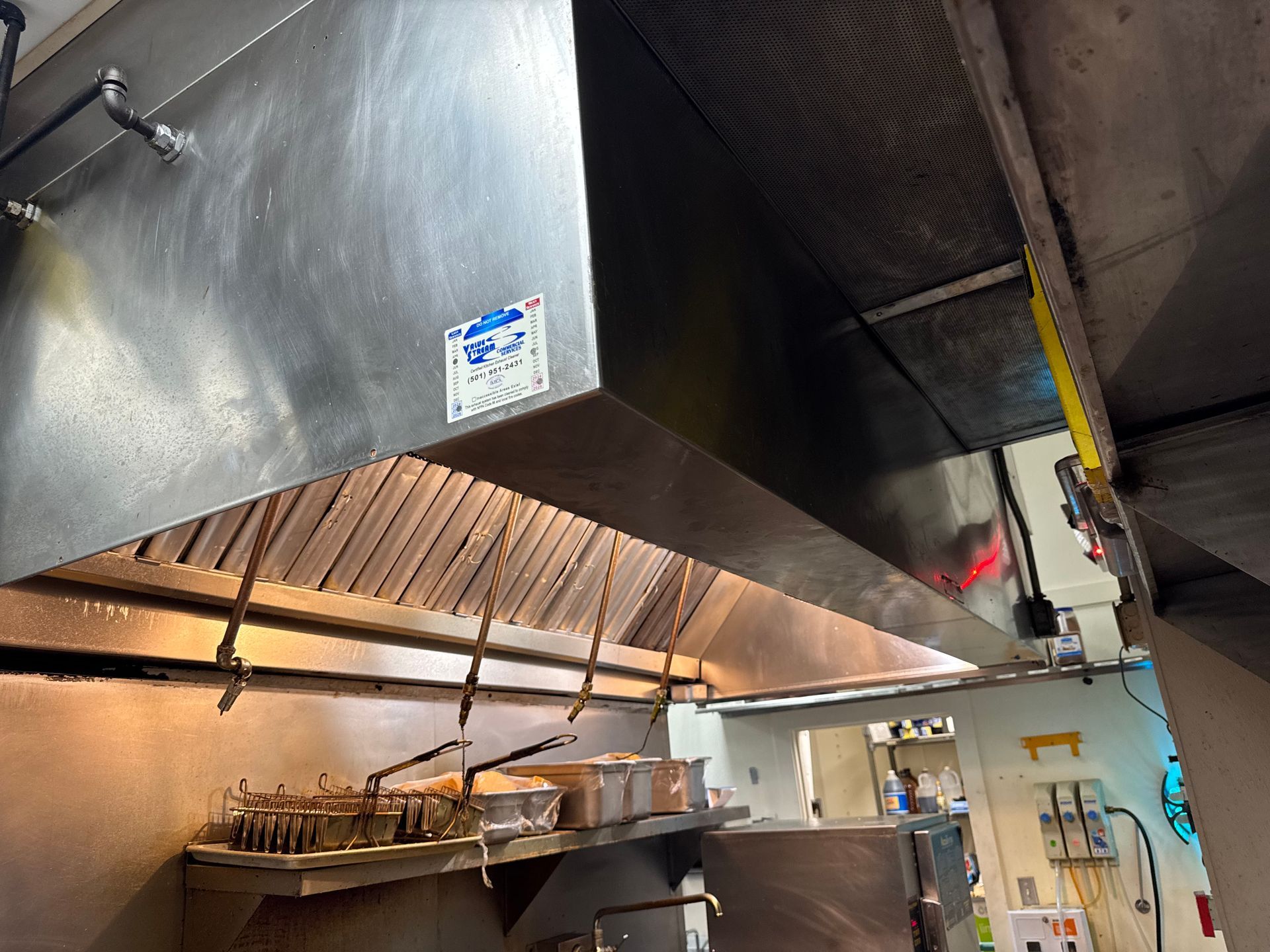 Stainless steel commercial kitchen exhaust hood above cooking equipment.