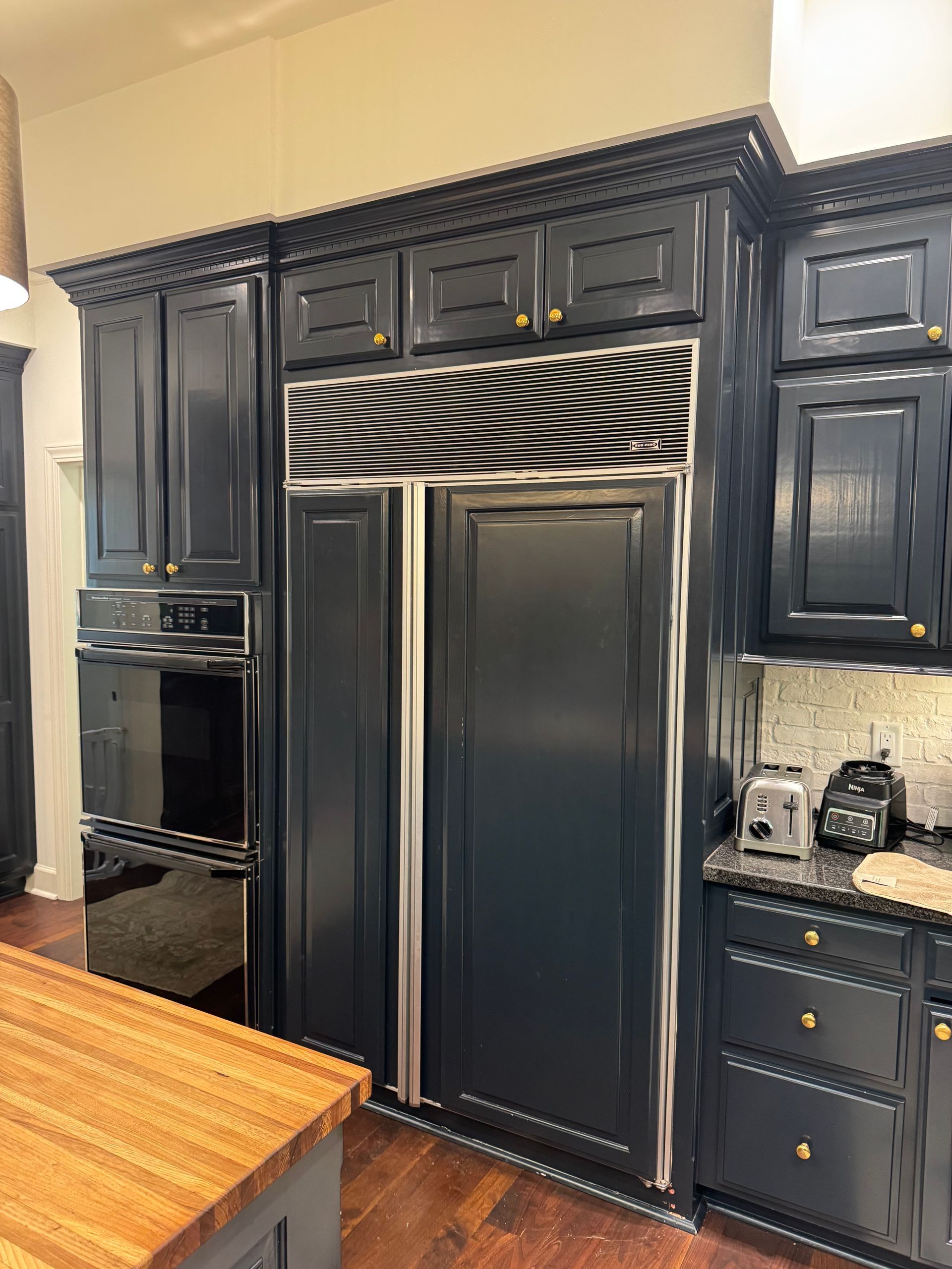 Dark blue kitchen cabinets with built-in oven, refrigerator, and countertop with gold hardware.