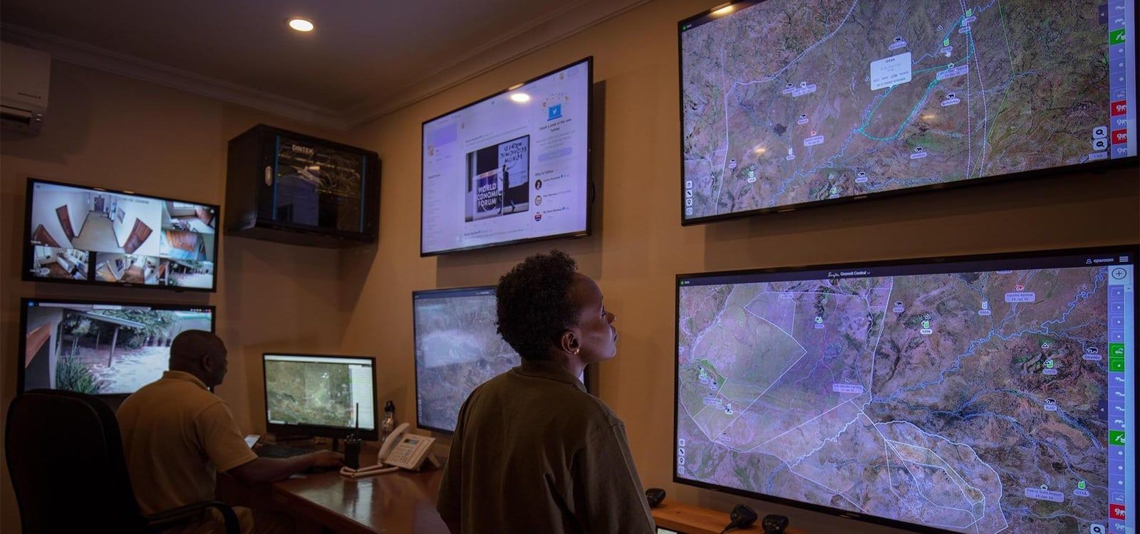 A man is standing in front of a bunch of monitors in a room.