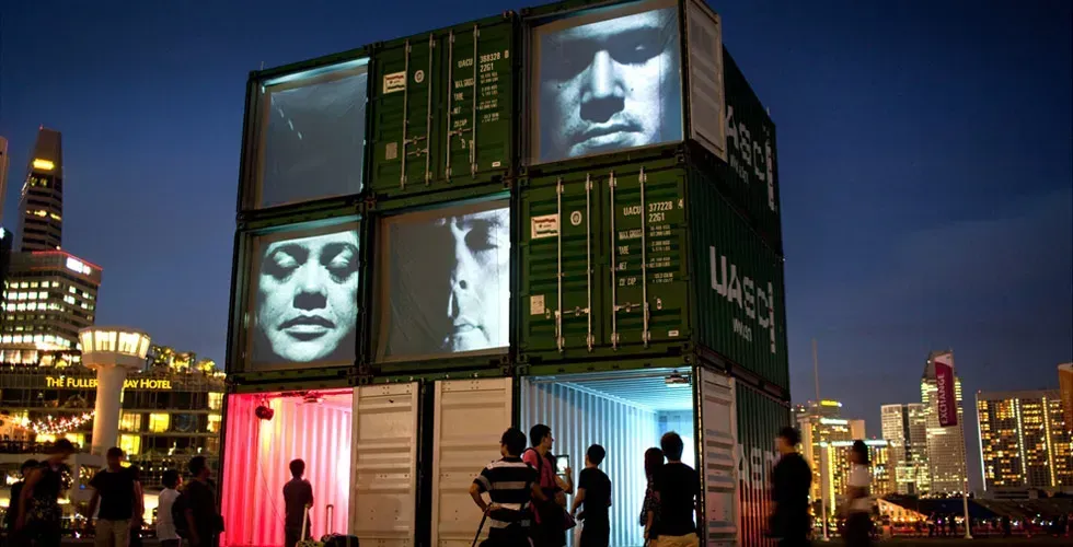 A group of people are standing in front of a building made out of shipping containers.