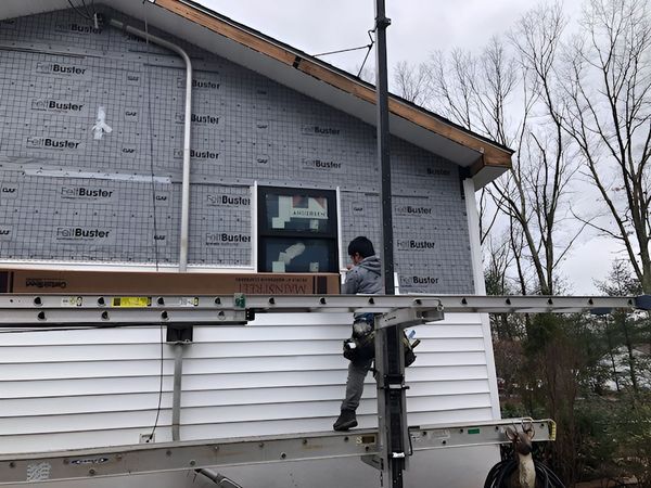 A man is climbing a ladder to install a window on the side of a house.