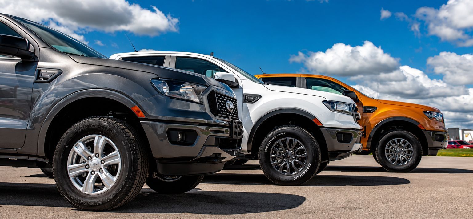 Three pickup trucks in black, white, and orange parked side by side under a blue sky