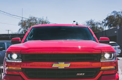 Front view of a bright red Chevrolet Silverado truck with headlights on outdoors