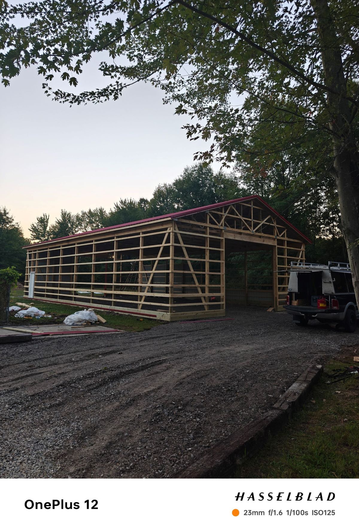Wooden building frame under construction with trees in the background. A gravel driveway is in the foreground.