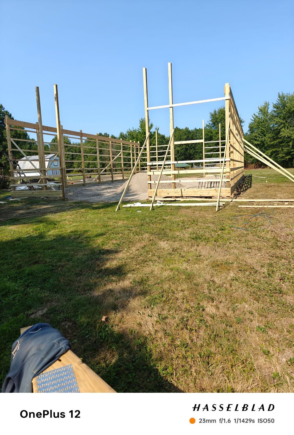 Wooden barn frame under construction on a grassy lot, with a clear blue sky in the background.